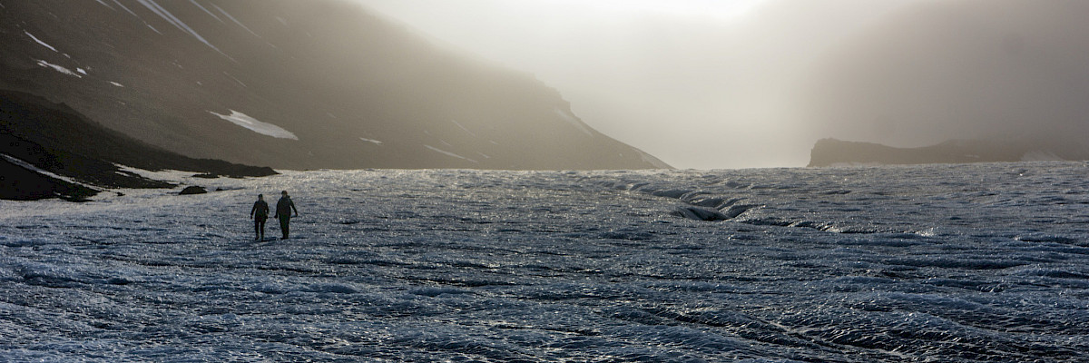 Two hikers are descending the glacier toward Longyearbyen.